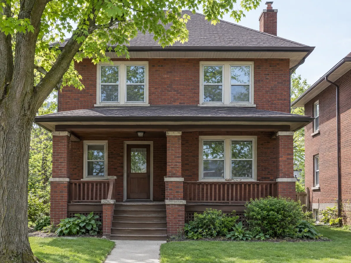 Red-brick 1920s foursquare with wood double-hung windows behind aluminium storms and a deep front porch