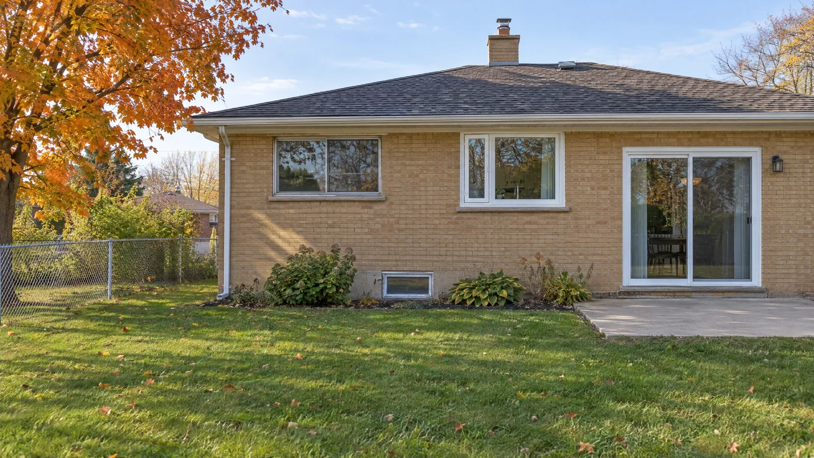 Back of a 1950s buff-brick bungalow with aluminium sliders, a white vinyl casement, a sliding patio door and a basement window