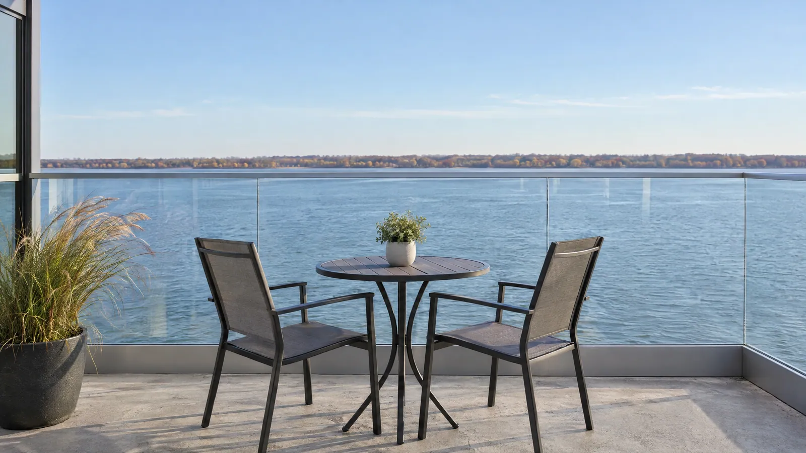Condo balcony with clear glass guard panels under a slim top rail, looking out over a calm river on an autumn day