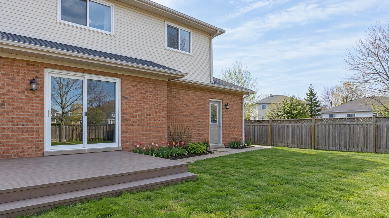 Rear of a 1990s brick and vinyl home with a sliding patio door onto a deck and a side door with a glass insert