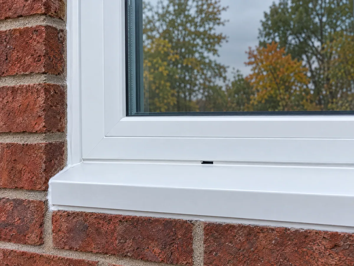 White aluminium capping wrapped over an old sill beneath a new vinyl window, with a tidy sealant joint against weathered red brick