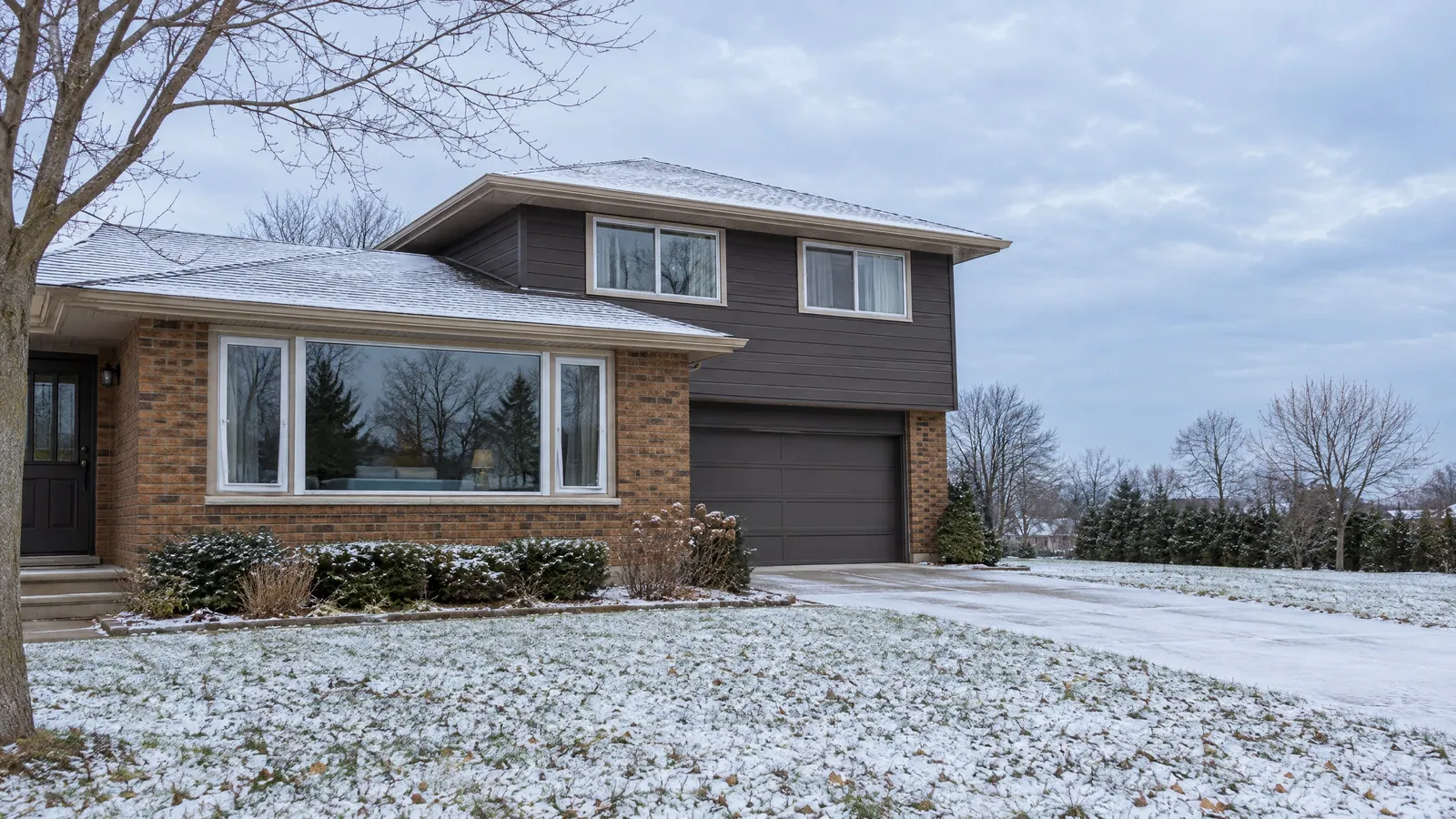1970s brick side-split with a large three-part picture window below, two sliders upstairs and light snow on the lawn
